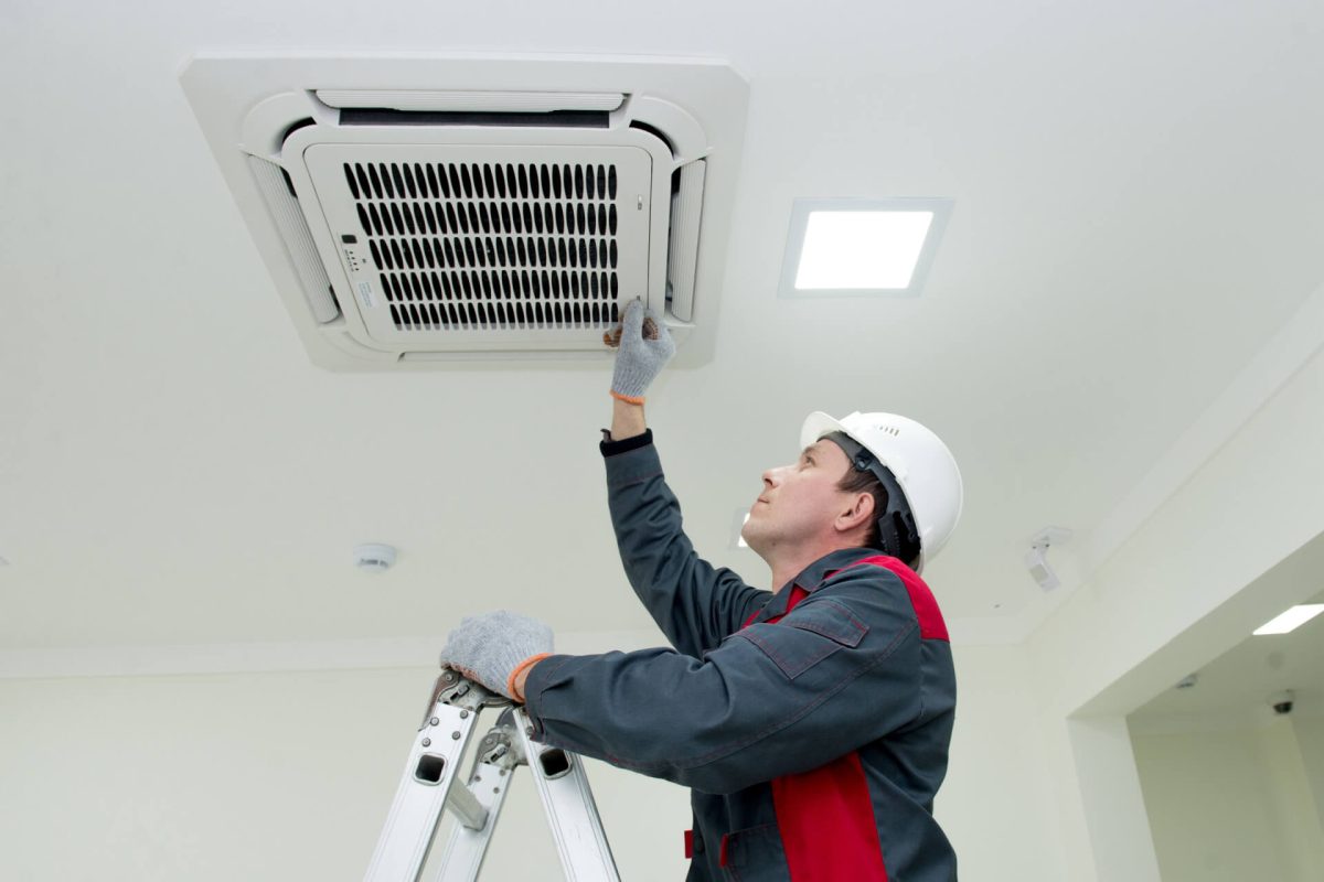 Technician cleaning or installing ceiling-mounted air conditioning unit.