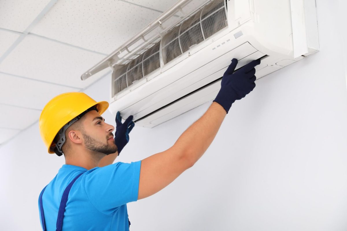 Technician removing dirty filter from wall-mounted AC unit.