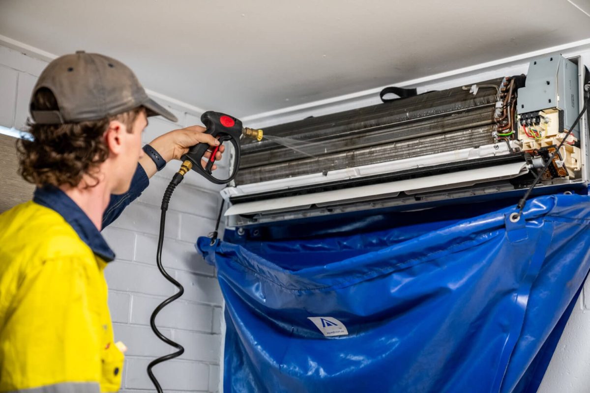 Technician using power tools to clean air conditioning unit with collection bag.