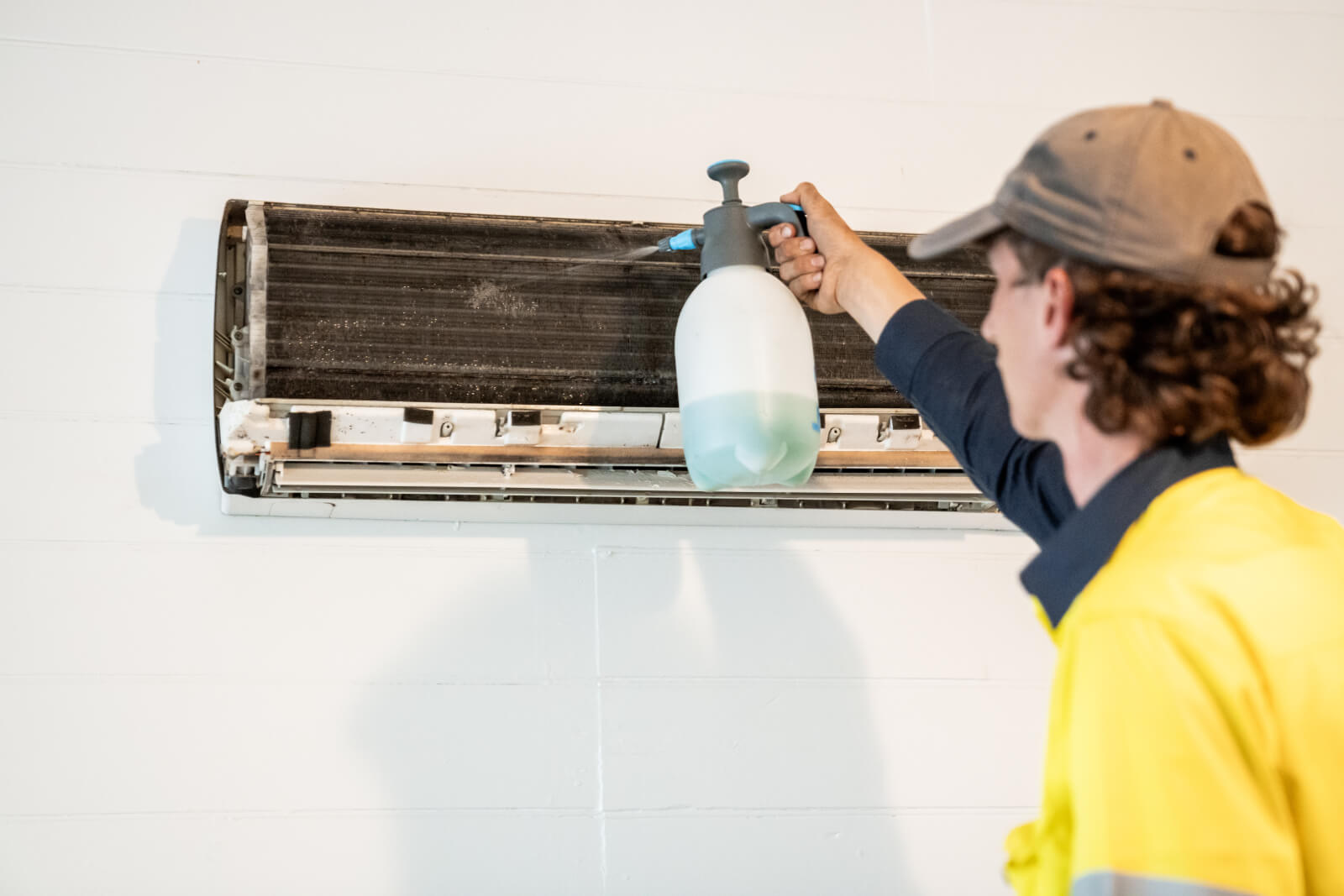 Technician cleaning a heavily soiled indoor air conditioning unit.