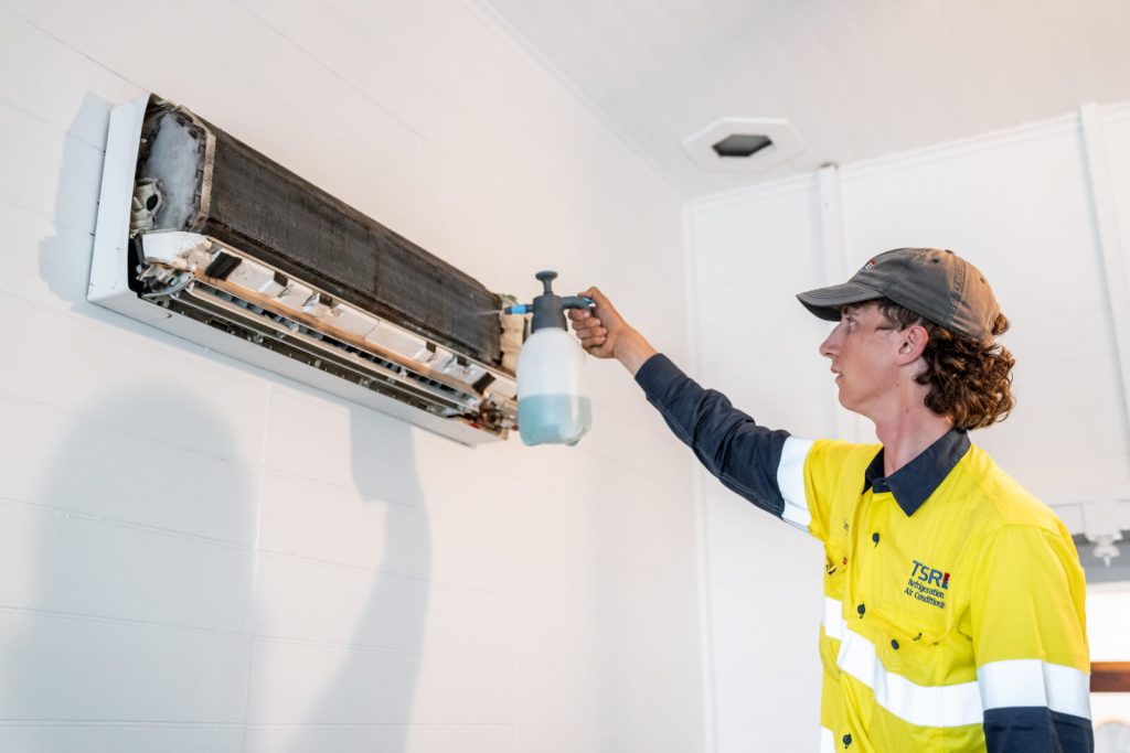 TSR technician spraying cleaning fluid onto a split system unit.